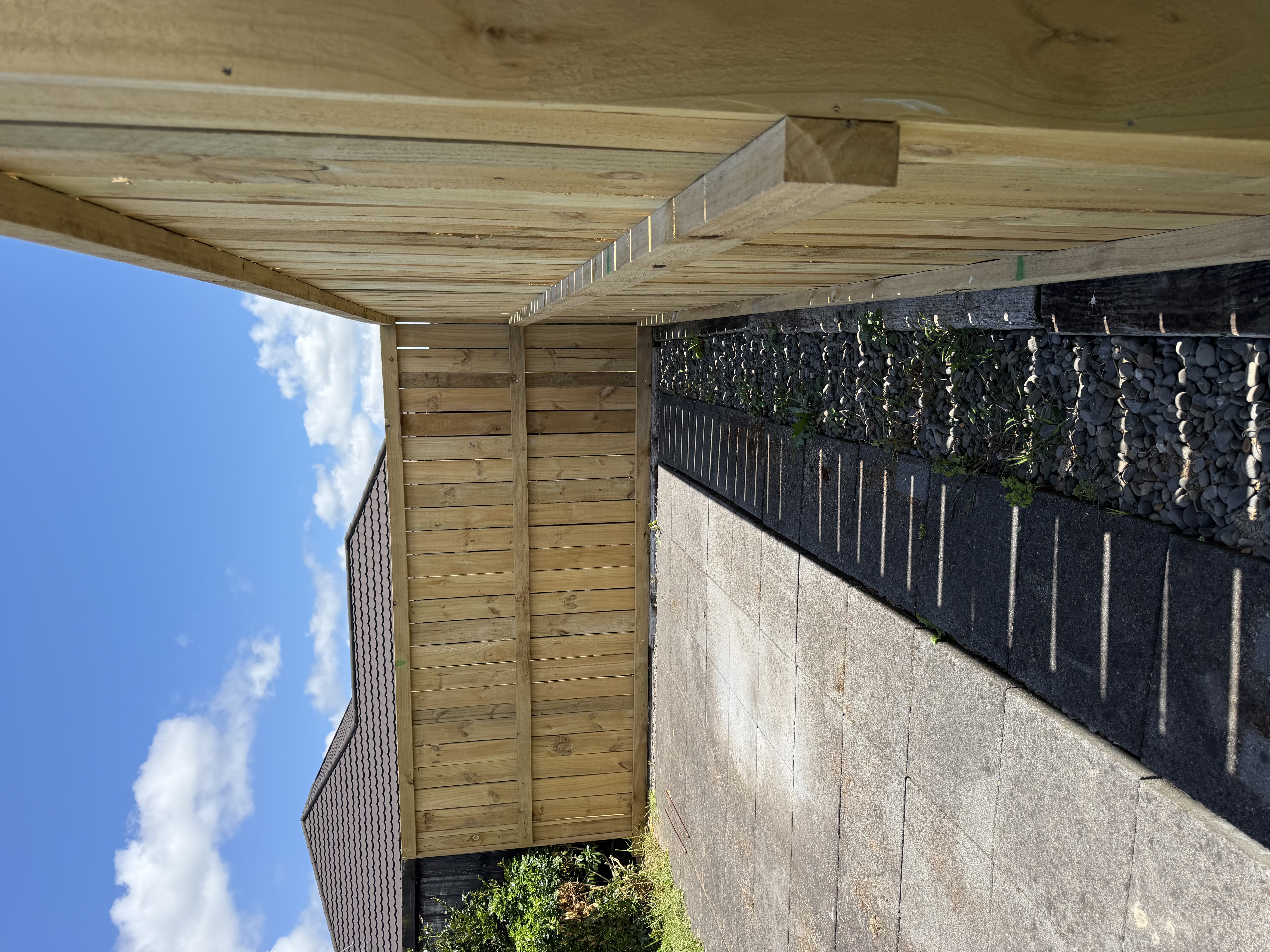 Timber boundary fence with black-pebble garden bed — Element Landscaping Waikato